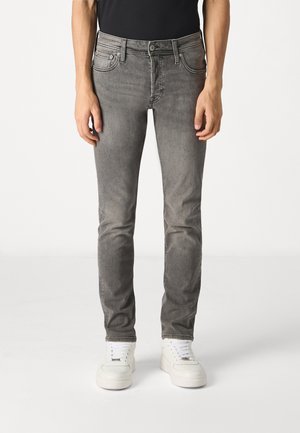 Jean en denim gris avec une coupe slim, dotés de cinq poches, d'un bouton en métal et de passants de ceinture. Associés à des baskets blanches pour un contraste.