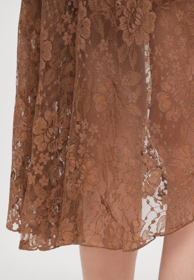 Un tissu en dentelle brune avec des motifs floraux tombe en douceur, mettant en valeur une texture semi-transparente et un en détail complexe dans le design.