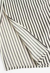 Tissu blanc avec des rayures verticales noires, plié pour montrer la direction contrastée des rayures et les détails de la texture.