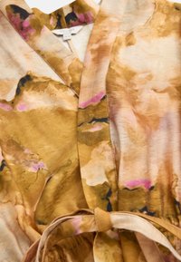 Damenkleid mit V-Ausschnitt, braun-beigem und pinkem Batikmuster und passendem Stoffgürtel, der in der Taille gebunden ist.