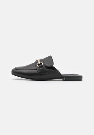Mule en cuir noir à enfiler, avec bout pointu et boucle argentée décorative sur la bride supérieure, semelle plate.