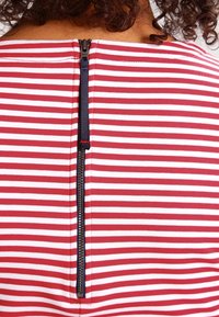 Röd och vit randig tröja med en marinblå dragkedja i ryggen, tillverkad av ett mjukt tyg med en figurnära design.