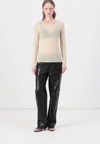 Beige, langermet, gjennomsiktig topp med V-hals; kombinert med høyt liv, sorte, imitert lærbukser. Minimalistisk design, glatt tekstur.
