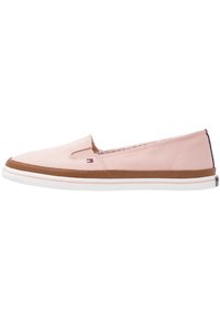 Zapato sin cordones de color rosa claro con parte superior de tela lisa, entresuela blanca y suela marrón. Cuenta con un pequeño logo y detalles cosidos.