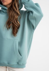Felpa oversize di un verde acqua chiaro con tasca a marsupio, polsini a coste e cappuccio con cordini, realizzata in un tessuto morbido e liscio.