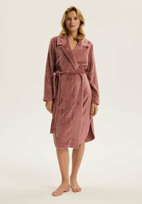 Różowy, teksturowany szlafrok z kołnierzem szalowym, długimi rękawami i paskiem. Posiada zygzakowaty wzór i sięga do długości połowy łydki.