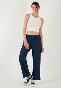 Bílý žebrovaný crop top v kombinaci s námořnickými širokými kalhotami. Kalhoty mají stahovací pas. Tenisky jsou námořnické s bílými akcenty.