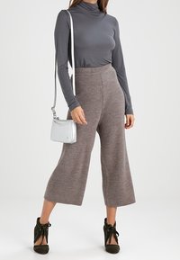 Szary golf, beżowe szerokie spodnie prążkowane, ciemnozielone buty na obcasie i mała srebrna torebka na ramię. Gładkie i teksturowane materiały.