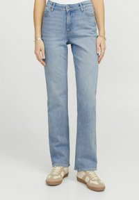 Svijetloplave traperice s ravnim nogavicama, pet džepova i pojasom na dugme. U kombinaciji s bež i bijelim tenisicama.