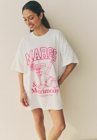 Vit oversized t-shirt med en livlig rosa grafisk utskrift av ett cocktailglas, ringar och texten "MARGS & Matrimony Bachelorette Club."