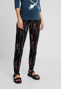 Černé kalhoty s vzorem v vertikálních pruzích v béžové, rezavé a tyrkysové barvě. Noseny s námořnickou blůzou a černými sandály s jednoduchým páskovým designem.