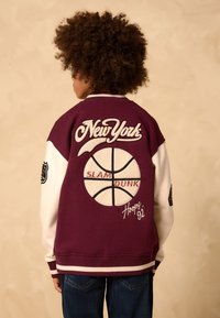 Bordeauxrotes College-Jackett mit weißen Ärmeln; verziert mit besticktem "New York", einem Basketballgrafik, den Details "SLAM DUNK" und "Hoops '92".