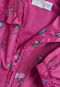 Giacca sintetica rosa con design di fragole e ciliegie, bordi arricciati e chiusura con zip. Fodera interna morbida con polsini elastici.