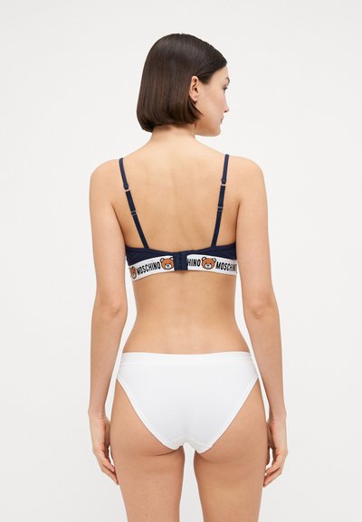 Navy bra with adjustable straps and bear logo band, paired with white bikini bottoms. Smooth fabric and minimalistic design.