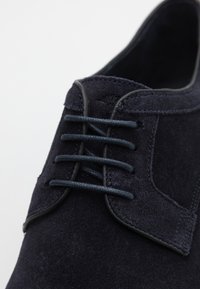 Scarpa in suede blu navy con punta tondeggiante, superficie testurizzata e chiusura con lacci a cinque occhielli, arricchita da accenti a contrasto lisci.