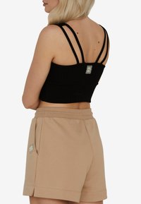 Czarny prążkowany crop top z wieloma cienkimi ramiączkami i kwadratową metką. W połączeniu z beżowymi szortami z bocznymi kieszeniami i małym akcentem logo.