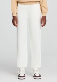 Białe dresowe spodnie o luźnym kroju, z elastycznymi mankietami i gładką fakturą, w połączeniu z białymi i brązowymi snekerami.