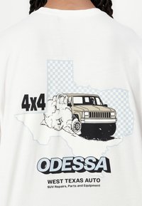 Biała koszulka z grafiką beżowego samochodu terenowego z dymem na niebieskiej szachownicy w kształcie Teksasu. Na koszulce napis "4x4" i "ODESSA".