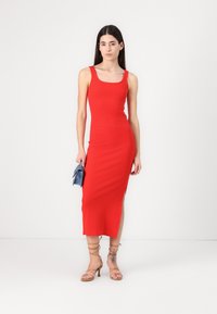 Red ribbed knit midi dress with a square neckline and side slit. Paired with tan lace-up heels and a small blue clutch.