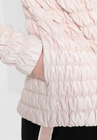 Giacca rosa voluminosa con texture arricciata, polsini elasticizzati e tasche laterali con dettagli in zip. Materiale sintetico morbido.