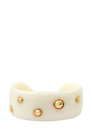 Bracelet large de couleur crème avec cinq clous ronds dorés uniformément espacés autour de lui sur un fond blanc.