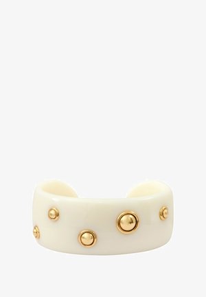 Bracelet large de couleur crème avec cinq clous ronds dorés uniformément espacés autour de lui sur un fond blanc.