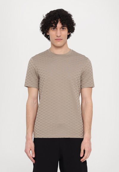 Beżowy t-shirt z teksturowanego materiału, z krótkimi rękawami i okrągłym dekoltem, z delikatnym wzorem z przodu oraz luźnym krojem.