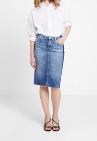 Denim pencil skirt in light blue with a front slit, frayed hem, paired with a white button-up shirt and strappy black heels.