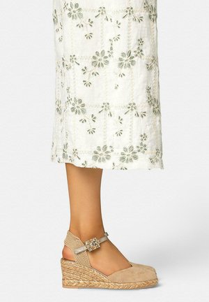 Alpargata beige de cuña con correa en el tobillo y hebilla decorativa, combinada con una falda midi blanca con bordados florales.