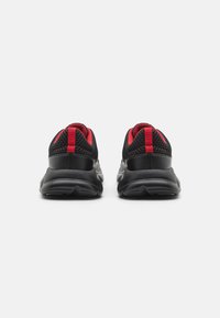 Chaussures de sport noires avec une tige en mesh, accents rouges, col rembourré et semelle en caoutchouc texturée, conçues pour le confort et le soutien.