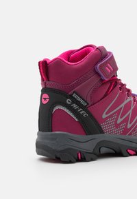 Mid-cut hiking boots in pink and gray with a waterproof upper, mesh lining, and textured rubber sole featuring grip patterns and accents.