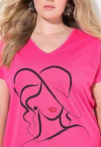 Fuchsie růžové tričko s výstřihem do V, se zapracovaným černým kresleným designem obličeje a rtů zdobených červenými rhinestony. Měkká textilie.