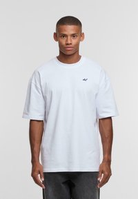 Camiseta de algodón blanca con corte oversized, mangas cortas, cuello redondo ribeteado y pequeño logo azul marino en el lado izquierdo del pecho. Tejido texturizado.