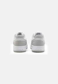 Zapatillas de deporte en gris y blanco con una parte superior de cuero suave, cuello acolchado y suela de goma con un patrón de banda de rodadura texturizado.