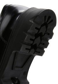Suola di scarpa in gomma nera con un motivo di battistrada testurizzato. Presenta scanalature prominenti e un tacco piatto per una migliore aderenza e durata.