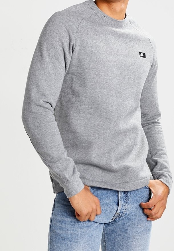 Harmaa huppari, jossa on pyöreä kaula-aukko, raglan-hihat ja pieni musta logopatchi rinnassa, yhdistettynä sinisiin farkkuihin.