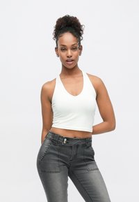 Valge lühendatud top sügava V-kaelusega, millel on tumehallid kõrge vöökohaga teksad nähtavate õmbluste ja taskutega.