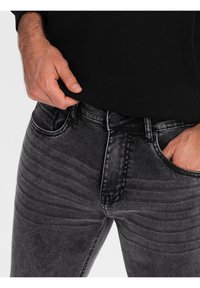 Jeans de mezclilla negra con un acabado desgastado, textura acanalada sutil, diseño de cinco bolsillos y cierre frontal con botón.