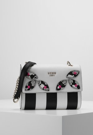 Sac à main rayé blanc et noir avec une bandoulière noire, orné de patches en forme de feuilles noirs et blancs avec des clous roses et le logo métallique "GUESS 1981".