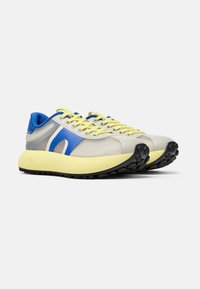 Sneakers sportivi con una tomaia in rete beige, rifiniture blu e gialle, lacci gialli e una suola intermedia spessa di colore giallo con una suola esterna nera testurizzata.
