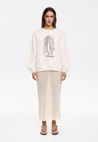 Sudadera de color beige claro con un estampado gráfico, combinada con una falda de punto texturizado en color crema. Chanclas negras completan el look.