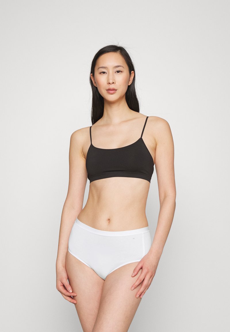 Camisola nera leggera con spalline sottili abbinata a slip bianchi a vita alta; entrambi gli articoli hanno una texture liscia e un design minimalista.