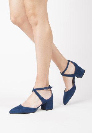 Marineblaue Wildleder-Heels mit spitzer Zehenform, Knöchelriemen und Blockabsatz. Glatte Textur mit minimalen Hardware-Details.