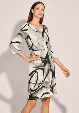Schwarz-weißes Kleid mit abstraktem Muster, dreiviertellangen Ärmeln, figurnaher Taille und einer Knoten-Detail am Bund, gefertigt aus einem glatten, elastischen Stoff.