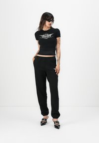Black short-sleeve crop top with silver graphic design, paired with black joggers and black heeled mules featuring straps and studs.