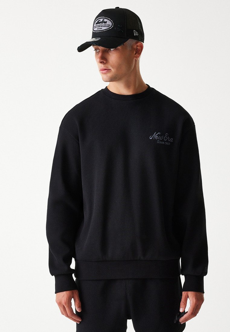 Schwarzer, gerippter Pullover mit langen Ärmeln, Rundhals und gesticktem "New Era"-Logo in Dunkelblau, kombiniert mit einer schwarzen Mesh-Cap.