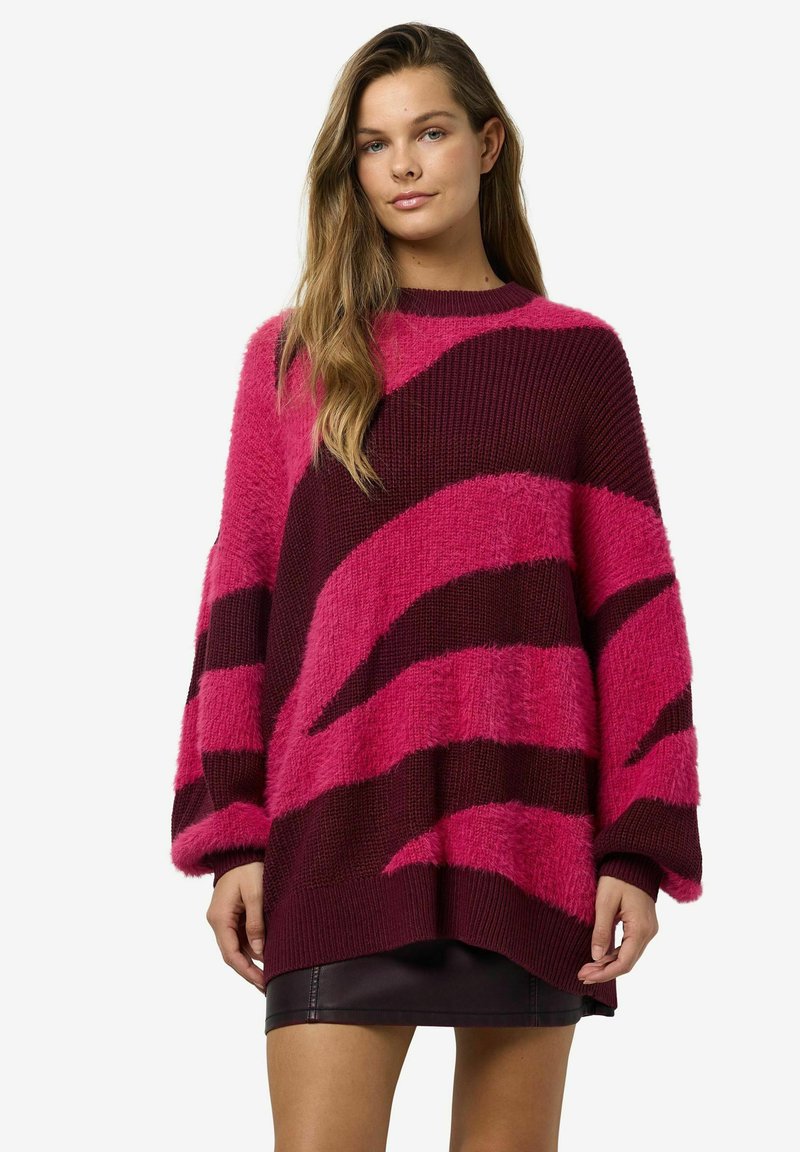 Liela izmēra džemperis fuksijas un bordo krāsā ar teksturētu, pūkainu virsmu. Iezīmējas ar drosmīgu diagonālu svītru rakstu un platām piedurknēm.