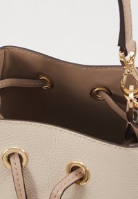 Sac seau en cuir beige clair avec quincaillerie dorée, doté d'un haut ouvert, d'une fermeture à cordon et d'une surface texturée.
