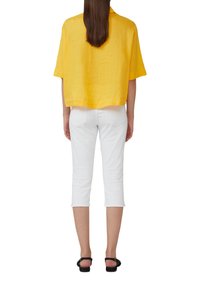 Haut jaune en lin à manches courtes avec une coupe ample, associé à un pantalon blanc court et des sandales noires, vu de dos.