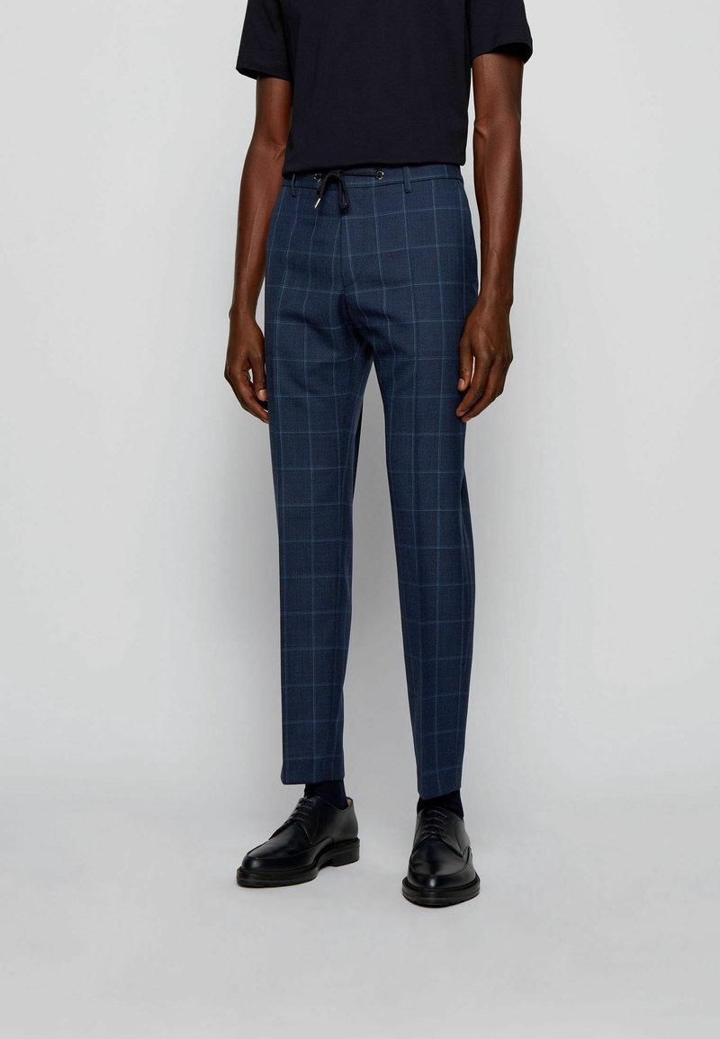 Námořnické kostkované kalhoty s přiléhavým střihem, s elastickým pasem, hladkou texturou a jemným kostkovaným vzorem. Nosit s černou košilí a botami.